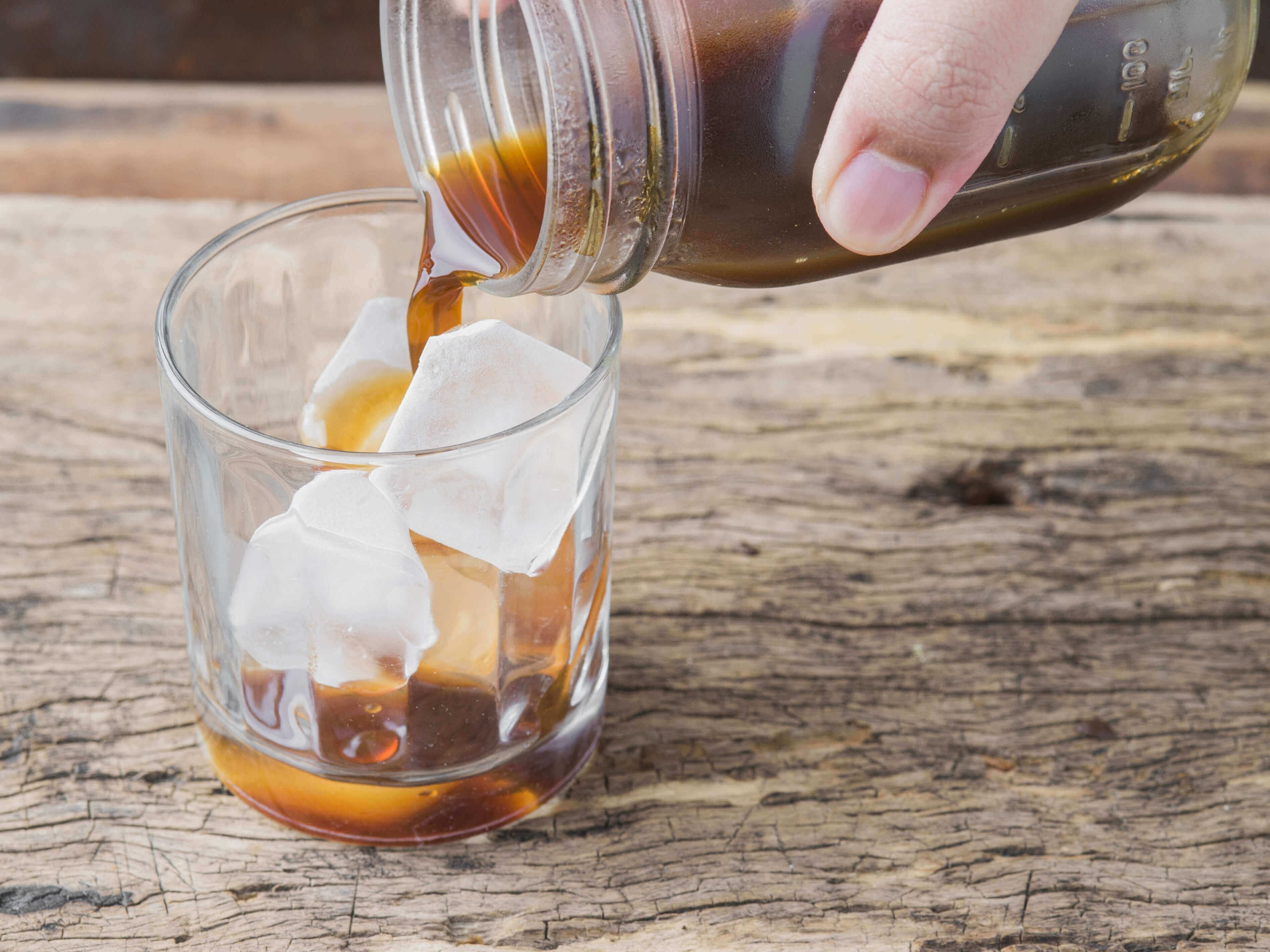 Close up of an old-fashioned glass that is filled with ice. Brown liquid is being poured into the glass.